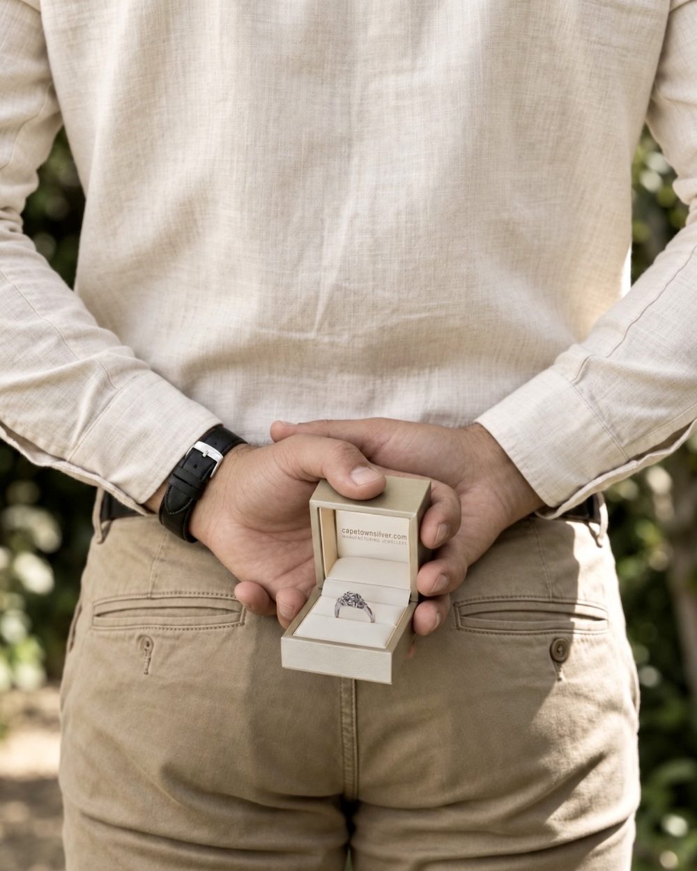 A man holding an open ring box behind his back, about to propose